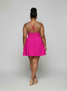 Person wearing a bright pink dress with thin straps on a plain background